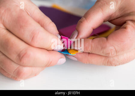 Ricamo e la trapuntatura in officina di un sarto donna - close-up sulle mani del sarto raccogliere dal desktop, scarti di tessuto colorato per pat Foto Stock