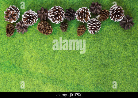 Pino e coni Fir sulla vibrante feltro verde dello sfondo con i fiocchi di neve. Decorazione per albero di natale Foto Stock