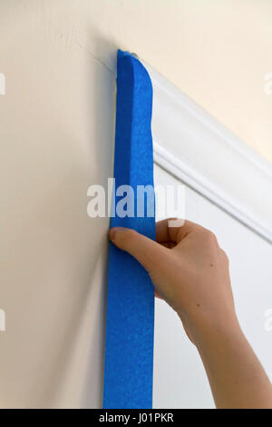 In prossimità di una giovane donna di applicazione a mano di colore blu del pittore il nastro su un telaio di porta prima della verniciatura di un muro adiacente Foto Stock