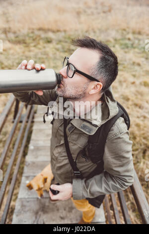 Escursionista in piedi sul ponte di legno con il suo cane e acqua potabile Foto Stock