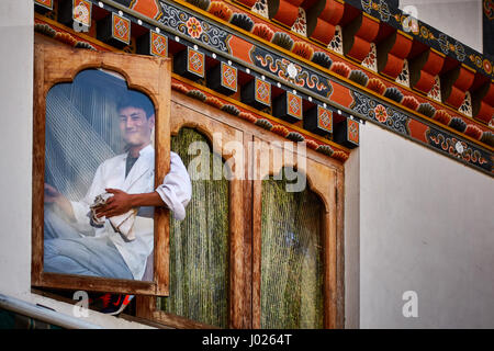 Un detergente per i vetri si siede sul davanzale della finestra la pulizia di una finestra di un edificio con architettura bhutanesi Foto Stock