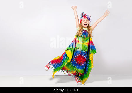 Felice bambino biondo ragazza in hippie abiti colorati contro il muro bianco Foto Stock