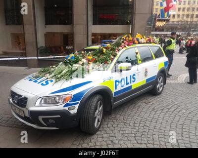 Polis svedese (polizia) auto parcheggiate in via centrale di Stoccolma, coperto da centinaia di mazzi di fiori, che simboleggia la svedese di generosa solidarietà e cordoglio per la perdita di vite umane dei loro compatrioti, dopo l'attacco terroristico con un carrello azionato da un uomo che indossa una felpa con cappuccio. Un uomo è stato arrestato nella misura dopo una caccia per il sospetto di pirata informatico che ha lasciato 4 morti e 16 feriti civili dietro le sue azioni. Foto Stock