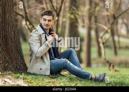 Moda uomo seduto accanto ad alberi con sfocatura sullo sfondo Foto Stock