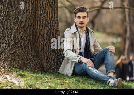 Moda uomo seduto accanto ad alberi con sfocatura sullo sfondo Foto Stock