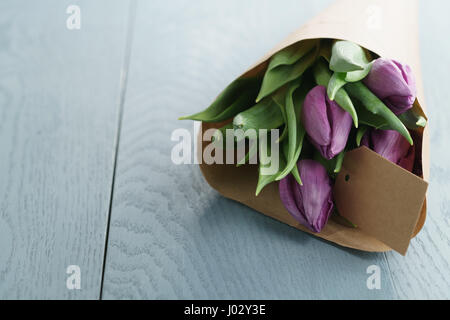 Viola i tulipani in imbarcazioni carta blu su uno sfondo di legno, con spazio di copia Foto Stock