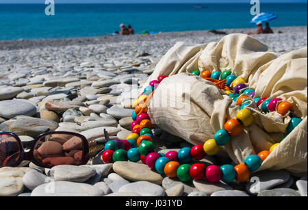 Borsa da spiaggia e occhiali da sole sulla spiaggia di ciottoli, tramonto Foto Stock