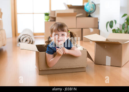 Ridere bambina seduta all'interno del cartone boxe nella sua nuova casa Foto Stock