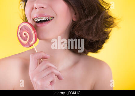 Giovane donna con multi-colore di staffaggio e candy in posa su sfondo giallo. Concetto dentale Foto Stock