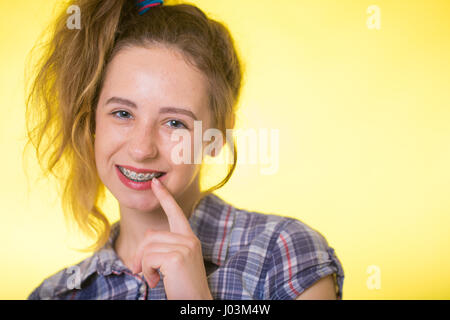 Giovane ragazza in un plaid shirt su sfondo giallo che mostra la sua parentesi dentale Foto Stock