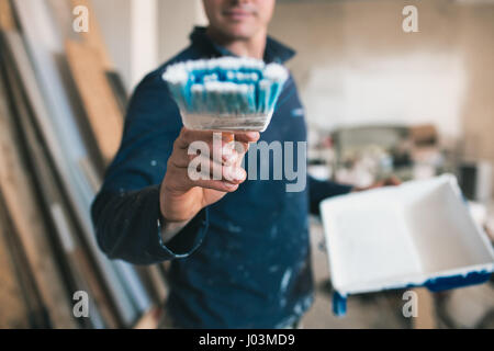 Il pittore in abiti da lavoro dipinge una parete immaginaria. Focus sulla spazzola Foto Stock