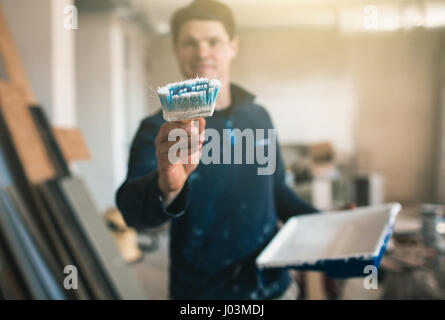 Il pittore in abiti da lavoro dipinge una parete immaginaria. Focus sulla spazzola Foto Stock