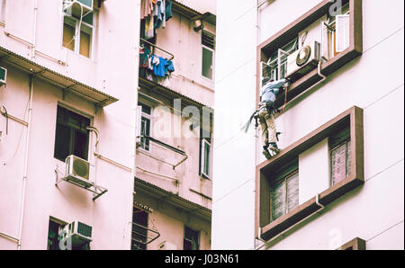 HONG KONG, CINA - 22 novembre 2016: una persona in piedi su una finestra e facendo il lavoro di manutenzione per il condizionatore d'aria. All'aperto orizzontale shot. Foto Stock