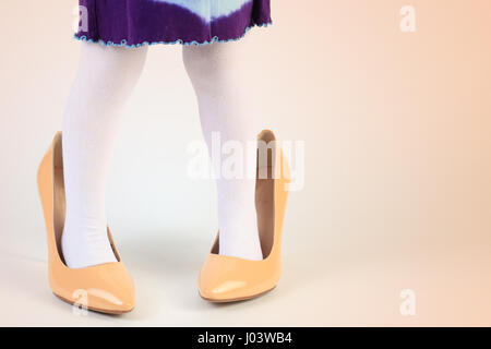 Bambino cercando sul tacco alto scarpe. Close-up del bambino in piedi in scarpe di colore giallo. Bambina gioca con la madre di scarpe. Funny bambino sfondo. Foto Stock