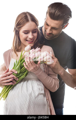 Giovane uomo abbracciando la donna incinta che holding bouquet di tulipani freschi Foto Stock