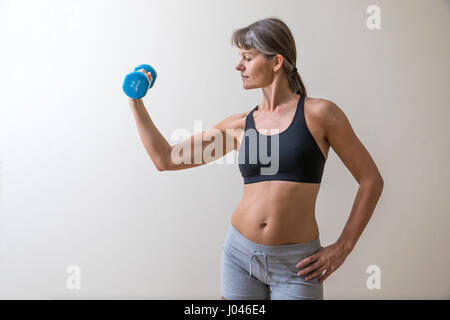 Donna di mezza età in palestra ingranaggio con un blu dumb bell. Foto Stock