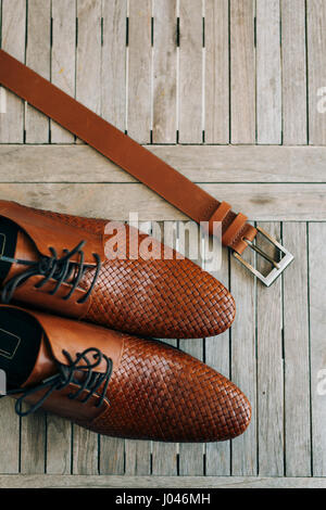 Brown uomo scarpe con lacci su uno sfondo di legno e una cintura marrone. Foto Stock