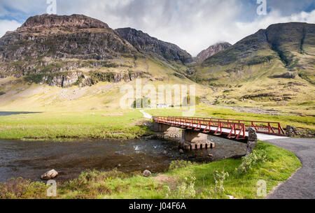 Un piccolo ponte che attraversa il fiume Coe al Cottage Achnambeithach accoccolato sotto le ripide montagne di Glen Coe in West Highlands della Scozia. Foto Stock