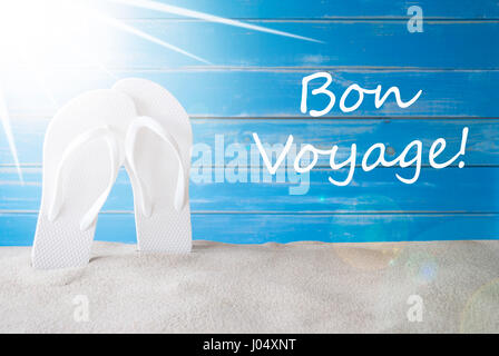 Testo francese Bon Voyage significa buon viaggio. Sunny Estate biglietto di auguri con sabbia e flip flop. Blue Vintage e Shabby Chic Sfondo di legno. Foto Stock