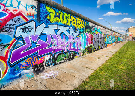 Vista panoramica del famoso muro di Berlino decorate con colorati graffiti street art alla storica East Side Gallery in una giornata di sole con cielo blu e nuvole Foto Stock