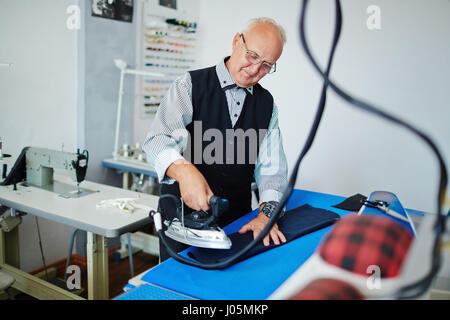 Senior uomo manicotto di stiratura della camicia nella sua Sartoria-shop Foto Stock