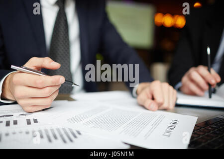 Closeup ritratto di due business irriconoscibile la gente vestita di nero abiti formali firma contratto le carte in tavola durante la riunione Foto Stock