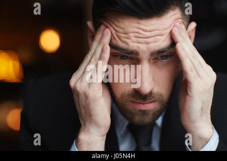 Ritratto di frustrati barbuto imprenditore strofinando il suo tempio ooking sottolineato e travagliato su sfondo nero Foto Stock