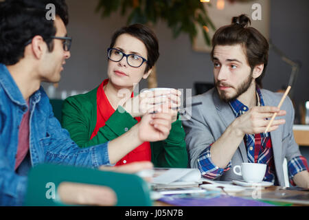 Un gruppo di giovani creativi collaborando alla riunione in cafe, parlare di lavoro e di idee di business, l'ascolto a un collega Foto Stock