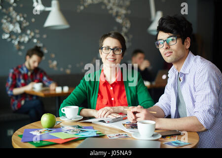 Ritratto di due informale giovani colleghi l uomo e la donna che indossa gli occhiali, discutendo di lavorare alla riunione di cafe e sorridente, guardando la fotocamera Foto Stock