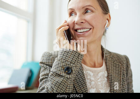 Donna felice con gli auricolari parlando sul telefono cellulare Foto Stock