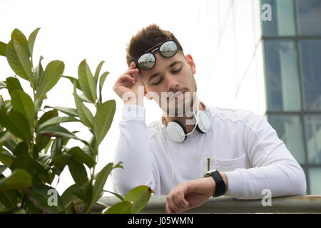 Bello e attraente giovane godendo all'aperto e guardando il suo orologio. Messa a fuoco selettiva e piccole profondità di campo. Foto Stock