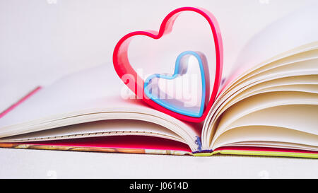Il rosso e il blu il cuore oltre il diario libro sul tavolo bianco Foto Stock