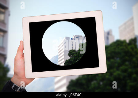 Mano maschile tenendo compressa contro l'angolo basso vista degli edifici della città Foto Stock