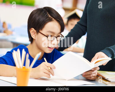 Asian scuola elementare studente ottenere aiuto da insegnante in classe. Foto Stock