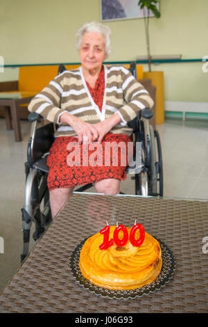 Vecchia donna in una casa di cura, su di lei un centinaio di compleanno con la sua festa di compleanno torta del. Foto Stock