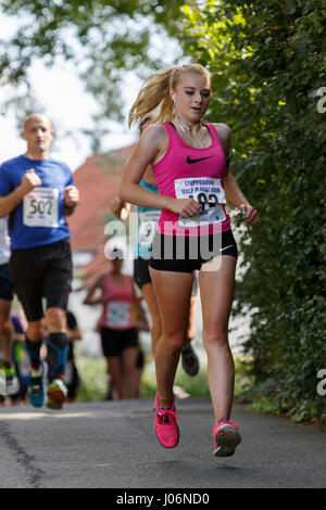 Una giovane donna / donna atleta che indossa in esecuzione abbigliamento sportivo è raffigurato in esecuzione in una mezza maratona corsa su strada in Chippenham, England, Regno Unito Foto Stock