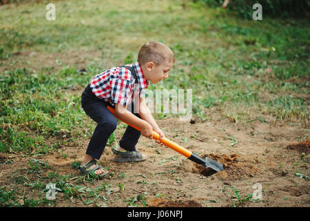 Piccolo ragazzo divertente con pala in giardino Foto Stock