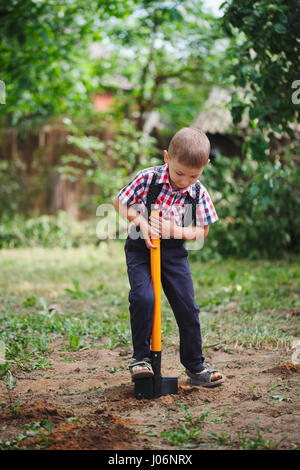 Piccolo ragazzo divertente con pala in giardino Foto Stock