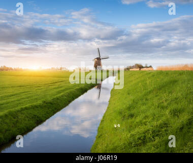 Mulini a vento di sunrise. Paesaggio agreste con mulini a vento olandese vicino all'acqua canali, erba verde e blu cielo nuvoloso riflessa nell'acqua. Bella morni Foto Stock
