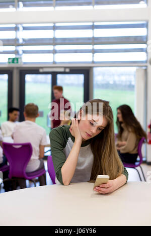 Studentessa seduta sul suo proprio a scuola. Ella ha uno smartphone in mano e ha sottolineato un espressione sul viso. Foto Stock