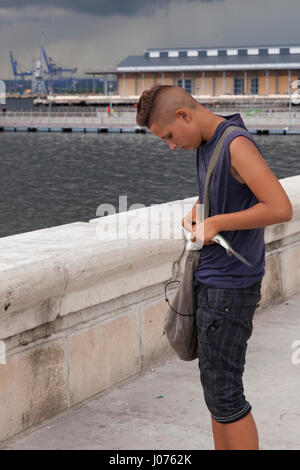 Un giovane rimuove cubano un gancio da un pesce di fronte al litorale lungo il Malecon in Old Havana, Cuba. Foto Stock