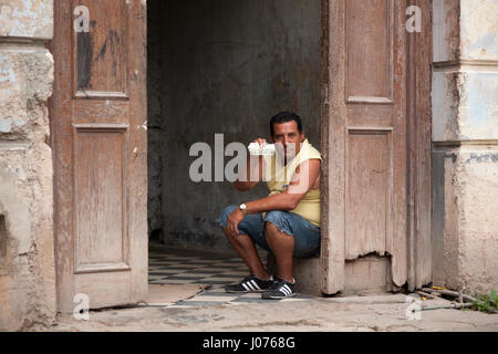Un uomo con un peso cubano seduto all'interno di un palazzo della vecchia Havana, Cuba. Foto Stock