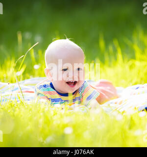 Adorable baby boy eating apple giocando sul manto colorato in verde erba. Bambino divertirsi sulla famiglia picnic nel giardino estivo. I bambini mangiano la frutta. Un sano Foto Stock