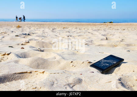 Telefono cellulare con schermo rotto in sabbia su una spiaggia, il fuoco selettivo. Foto Stock