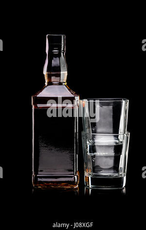 Bottiglia di whiskey con etichetta vuota e due bicchieri vuoti su sfondo nero Foto Stock