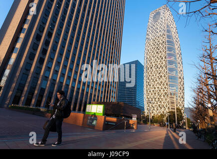 Un uomo giapponese che usa uno smartphone cammina vicino alla caratteristica Torre Cocoon a Shinjuku, Tokyo, Giappone. Foto Stock