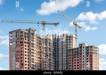 Incompiuta ad alto edificio di appartamenti e gru a torre sul cielo blu sullo sfondo Foto Stock