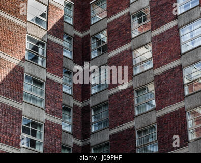 Un rosso-mattone di blocchi di appartamenti in corrispondenza di un angolo con riflessioni di frazioni in Windows Foto Stock