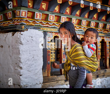 Una donna che porta un bambino gira ruote della preghiera sulla parete del Changangkha Lhakhang tempio a Thimphu Bhutan Foto Stock