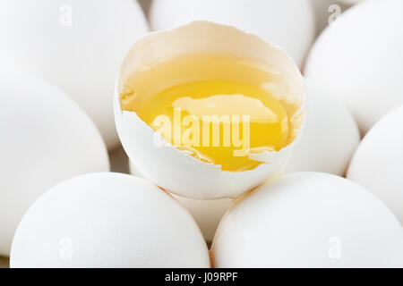 Chiudere su di uno sfondo di bianco fresco uova di pollo. Estrema profondità di campo con il fuoco selettivo su materie uova incrinate e tuorlo nella shell. Foto Stock